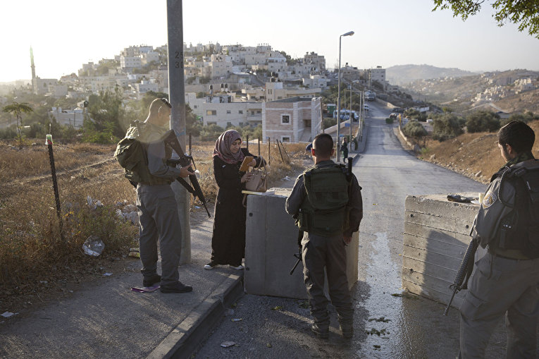 Израильские полицейские проверяют документы у палестинки рядом с бетонными блоками, установленными на востоке Иерусалима