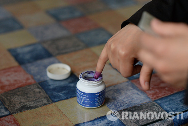 Женщина опускает палец в емкость с чернилами для отметки в списке избирателей во время голосования на парламентских выборов в Сирии