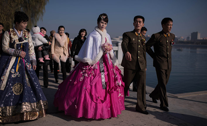 Жених и невеста с родственниками и друзьями ругяют на берегу реки Тэдон в Пхеньяне
