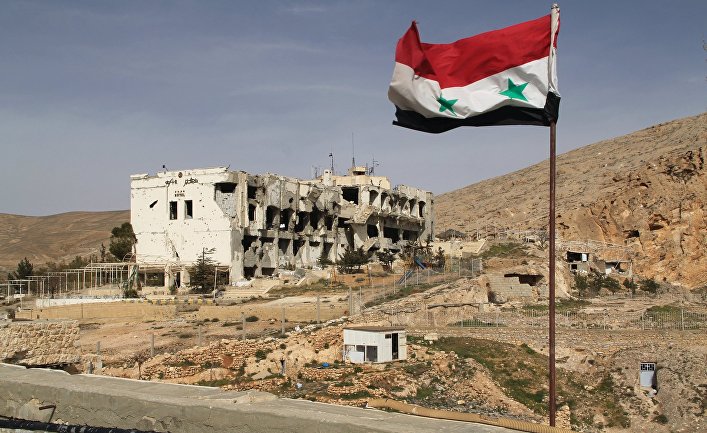 Сирийский флаг на фоне разрушенного дома в сирийском городе Маалюля в 55 км от Дамаска