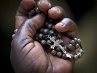 Женщина держит в руке распятие во время мессы в католическом храме в Кампалы в Уганде