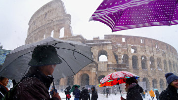 Люди с зонтами перед Колизеем во время снегопада в Риме, Италия