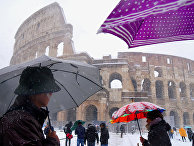 Люди с зонтами перед Колизеем во время снегопада в Риме, Италия