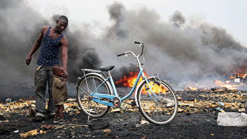Мужчина с ребенком стоят на фоне дыма в районе Агбогблоши (Agbogbloshie), составляющем агломерацию столицы Ганы
