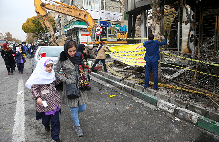 Люди в Тегеране идут мимо сгоревшего банка после протестов против повышения цен на топливо