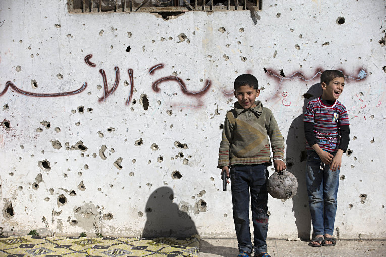 Сирийские мальчики играют в футбол возле разрушенных зданий в городе Хомс