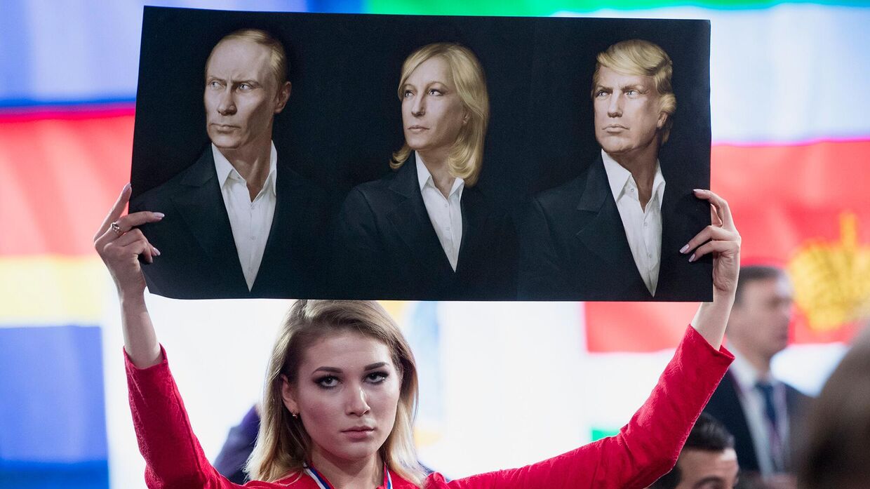 Журналист держит плакат с портретами Владимира Путина, Марин Ле Пен и Дональда Трампа