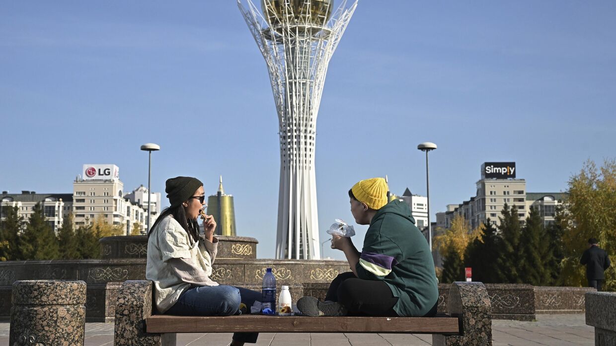 Молодые люди обедают на лавке возле монумента Астана-Байтерек в Астане, Казахстан