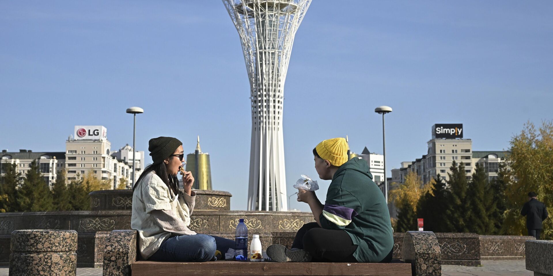 Молодые люди обедают на лавке возле монумента Астана-Байтерек в Астане, Казахстан - ИноСМИ, 1920, 21.03.2023