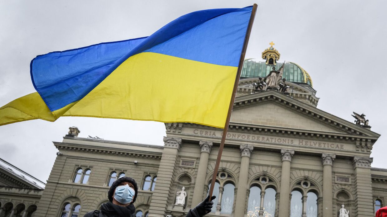 Мужчина размахивает украинским флагом перед зданием парламента Швейцарии в Берне