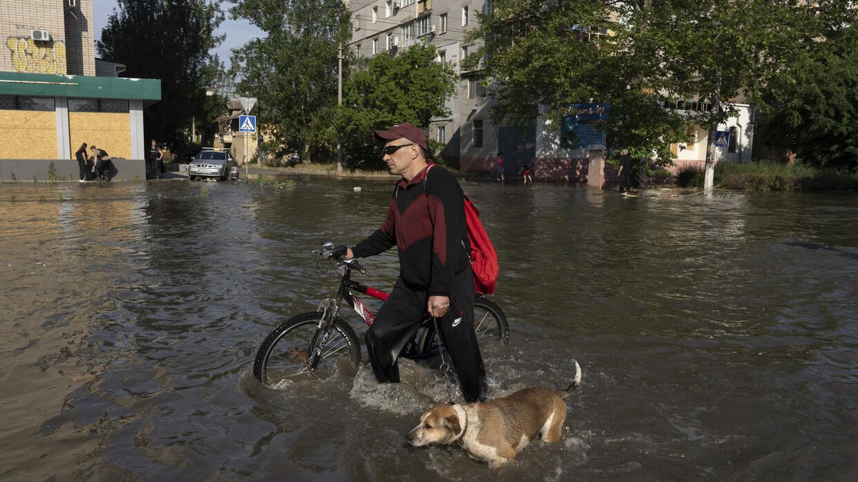 Местный житель с велосипедом и собакой идет по улице в Херсоне, Украина, во вторник, 6 июня 2023 года, которая была затоплена после взрыва плотины Каховской ГЭС