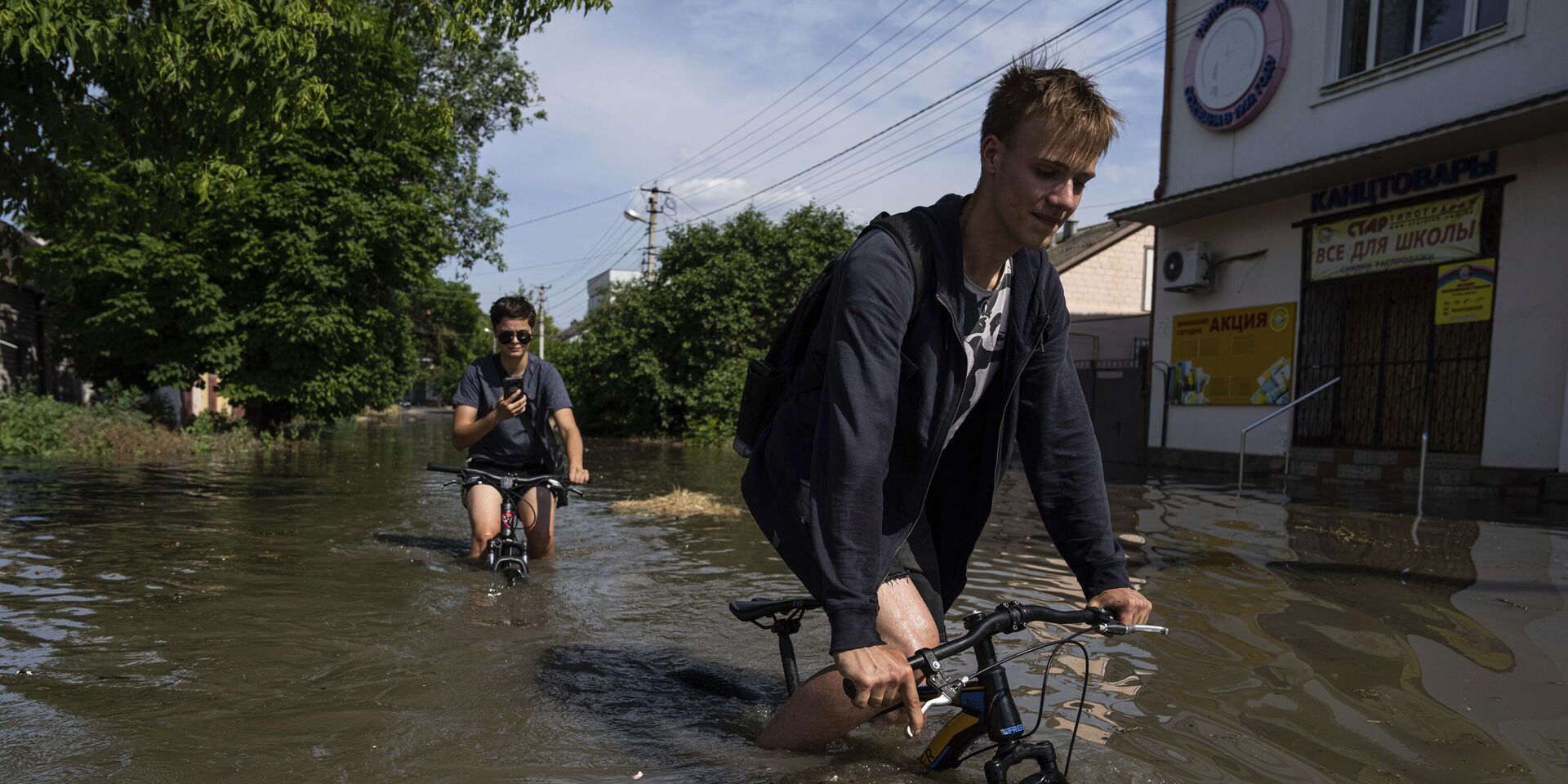 Местные жители пытаются проехать на велосипедах по затопленной дороге после прорыва плотины Каховской ГЭС в Херсоне, Украина, 6 июня 2023 года. - ИноСМИ, 1920, 09.06.2023