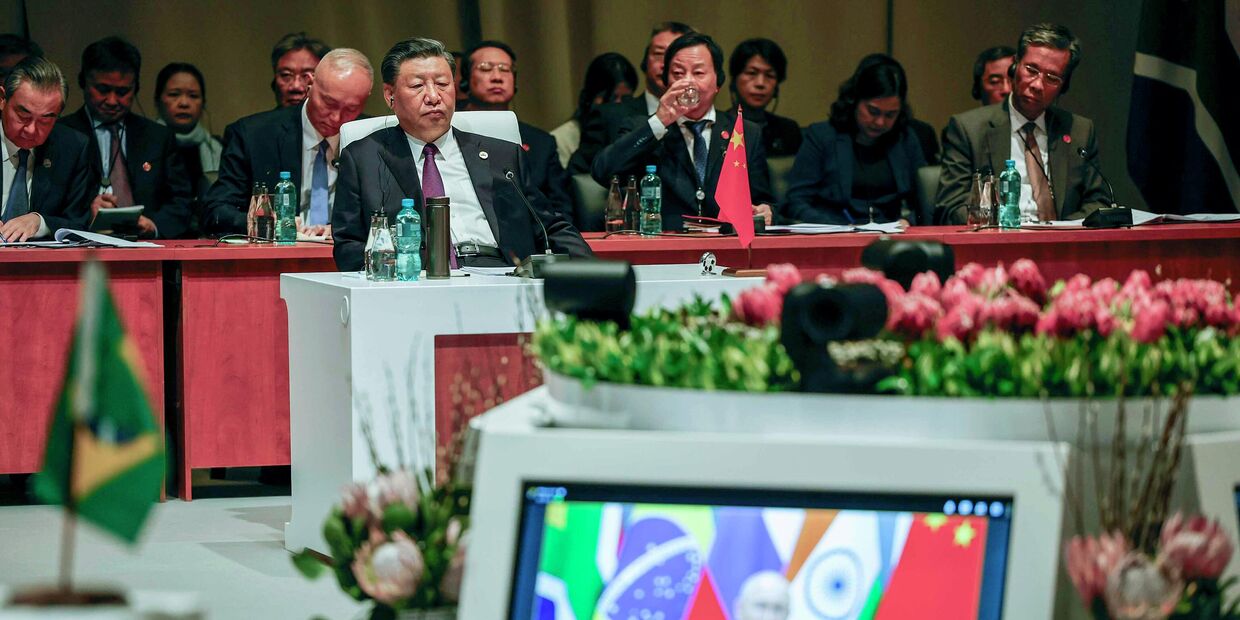 Председатель Китая Си Цзиньпин наблюдает за пленарным заседанием, в то время как президент России Владимир Путин выступает со своей речью по видеосвязи во время саммита БРИКС 2023 года в конференц-центре Сэндтон в Йоханнесбурге в среду, 23 августа 2023 года.