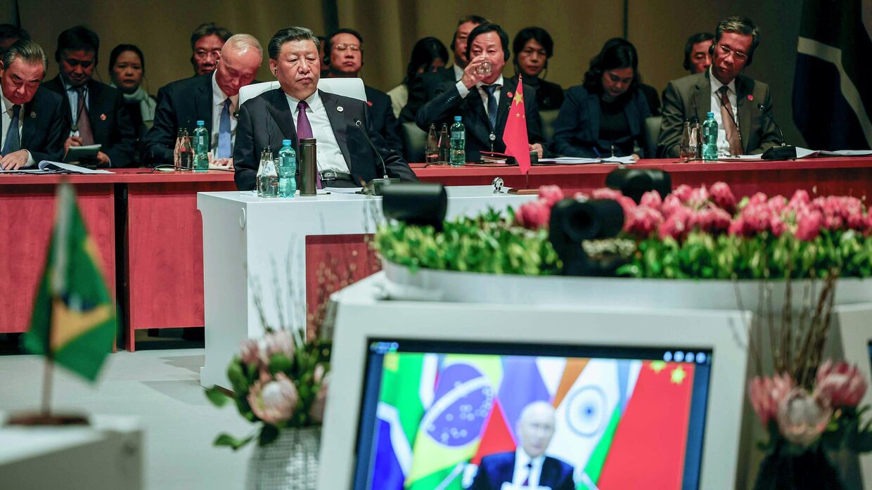 Председатель Китая Си Цзиньпин наблюдает за пленарным заседанием, в то время как президент России Владимир Путин выступает со своей речью по видеосвязи во время саммита БРИКС 2023 года в конференц-центре Сэндтон в Йоханнесбурге в среду, 23 августа 2023 года.