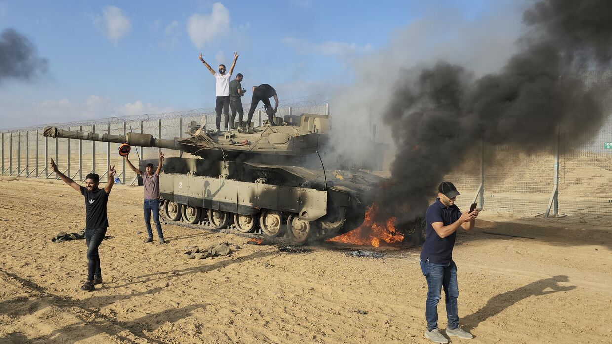 Палестинцы ликуют возле уничтоженного израильского танка рядом с ограждением сектора Газа  в субботу, 7 октября 2023 года