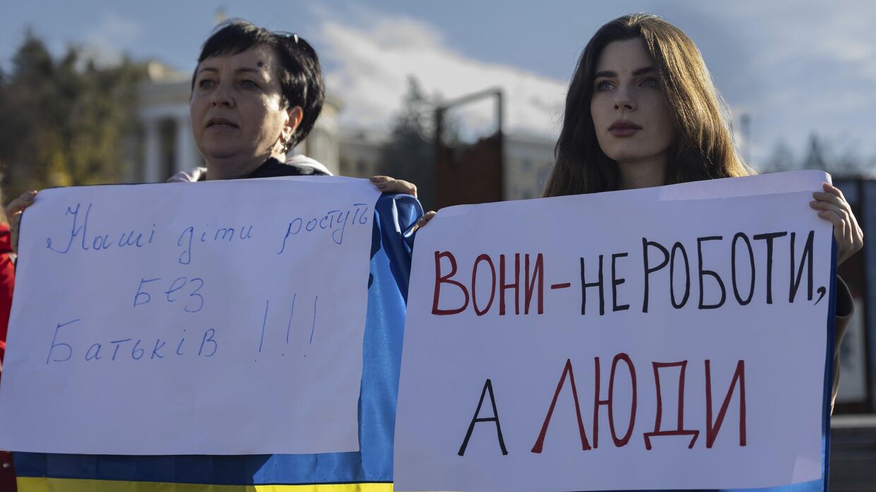 Мария Харченко, справа, которая ждет возвращения своего мужа с передовой, держит плакат с надписью Они не роботы, а люди во время митинга на площади Независимости в Киеве, 27 октября 2023 года.