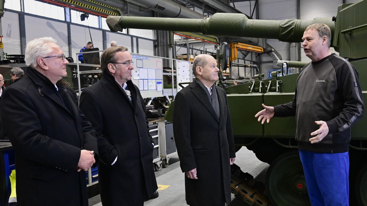 Канцлер Германии Олаф Шольц (в центре), министр обороны Борис Писториус (второй слева) в сопровождении генерального директора Rheinmetall Армина Паппергера (слева) беседуют с сотрудником на будущей площадке оружейного завода, где Rheinmetall планирует производить артиллерию с 2025 года