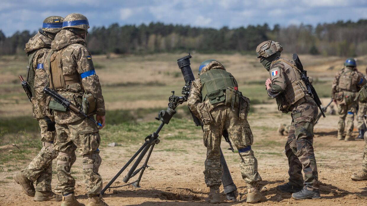 Инструктор французской армии (справа) проверяет миномет перед тем, как украинские солдаты начнут стрелять из него во время учений с французскими военными в военном учебном комплексе в Польше 4 апреля 2024 года