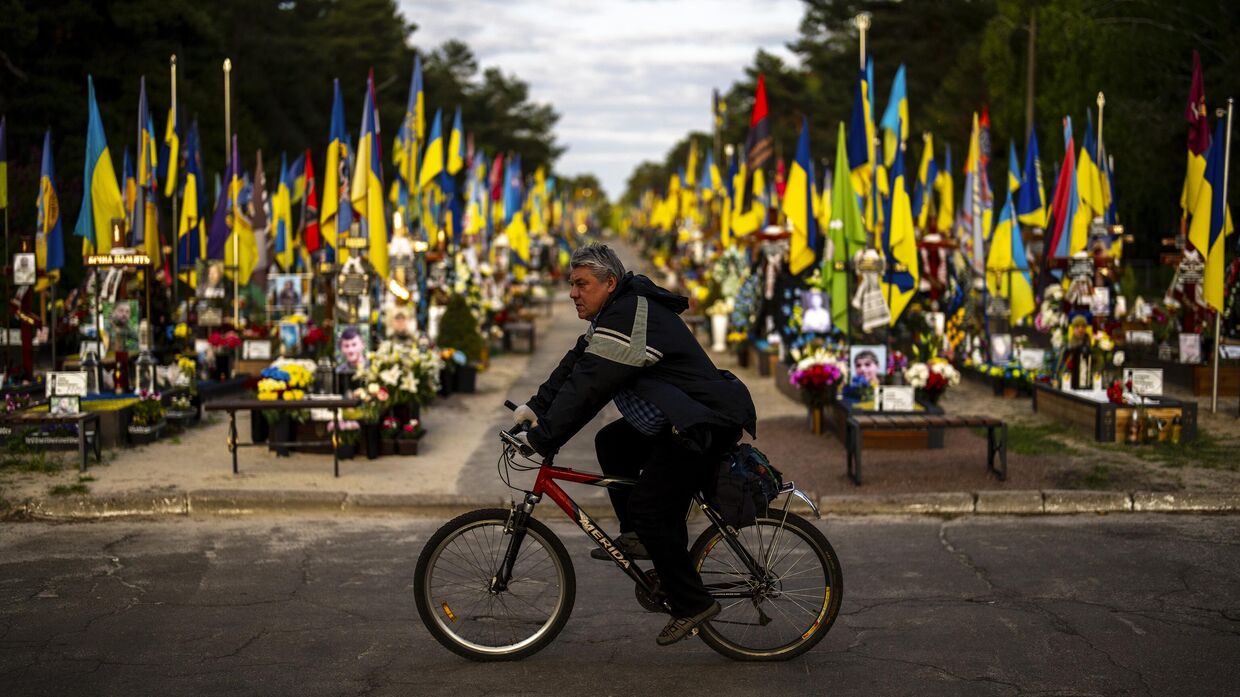 Велосипедист проезжает мимо могил украинских солдат, погибших во время боевых действий, на Лесном кладбище в Киеве