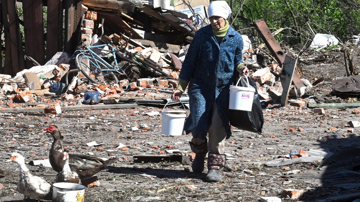 Женщина кормит уток во дворе поврежденного в результате обстрелов ВСУ жилого дома в поселке 1-й Лиман Харьковской области