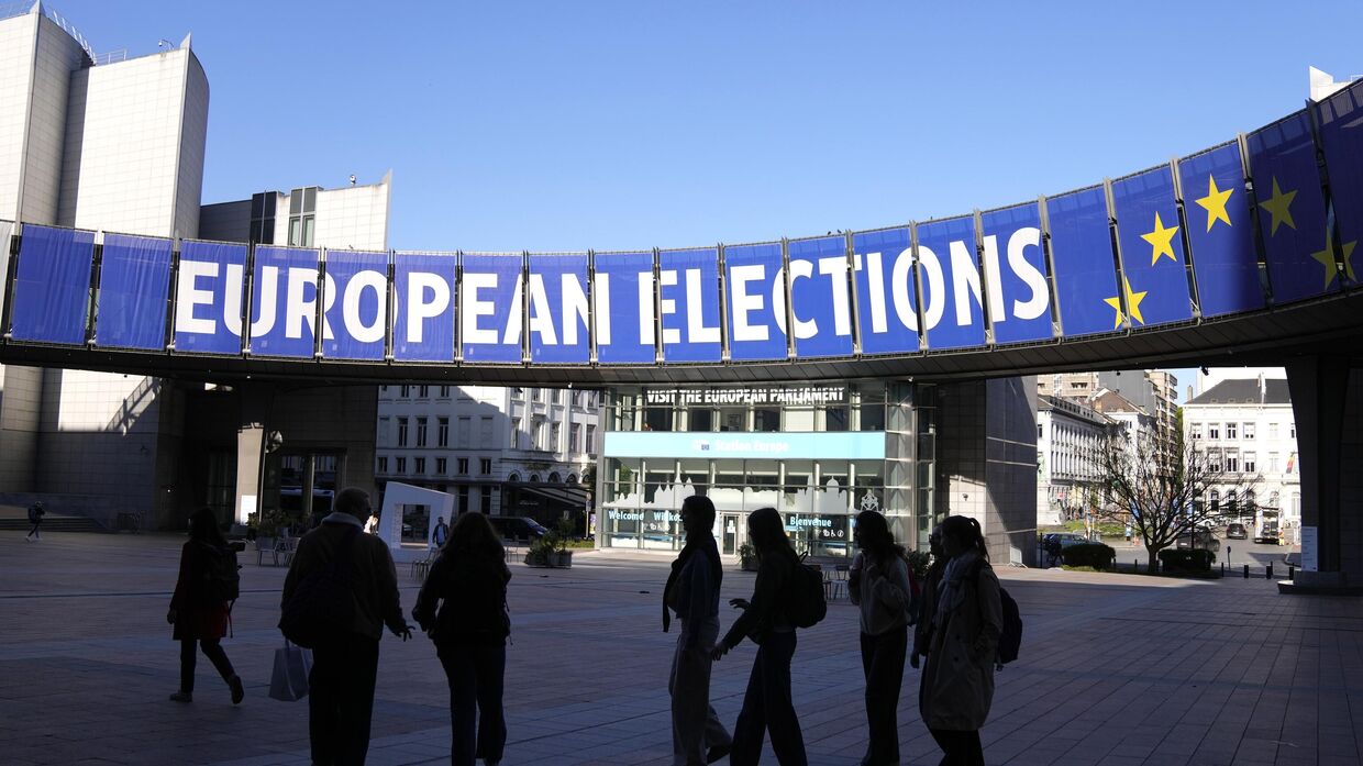 Группа людей стоит под предвыборным баннером у здания Европейского парламента в Брюсселе в понедельник, 29 апреля 2024 года. Европейские выборы пройдут с 6 по 9 июня 2024 года. 
