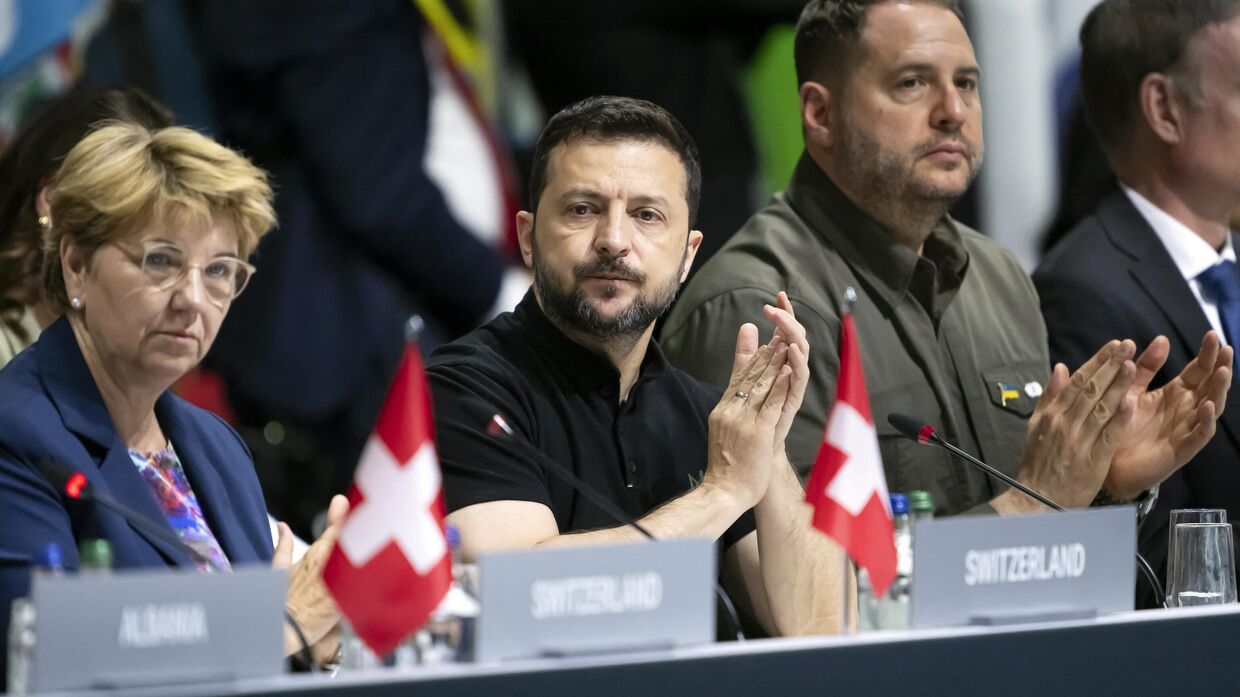 Владимир Зеленский аплодирует рядом с президентом Швейцарии Виолой Амхерд (слева) и главой Офиса Зеленского Андреем Ермаком во время пленарного заседания на саммите мира в Бургенштоке, 16 июня 2024 года.