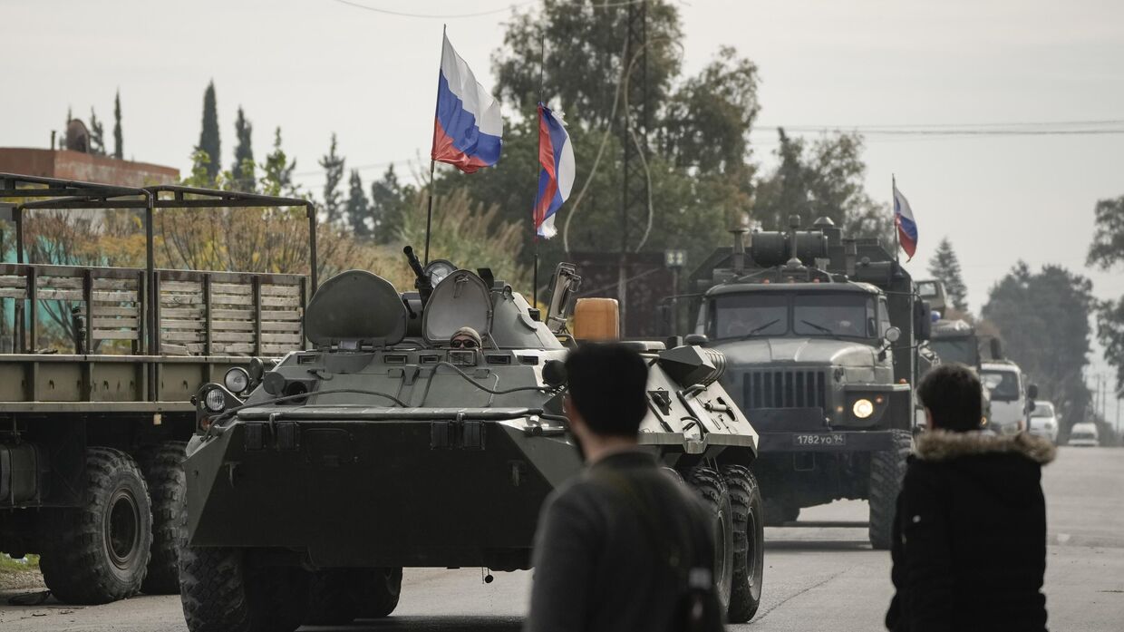 Сирийские боевики наблюдают за российской бронетехникой, проезжающей мимо авиабазы Хмеймим, которая в настоящее время находится под управлением России, в городе Хмеймим, Сирия, 16 декабря 2024 года.