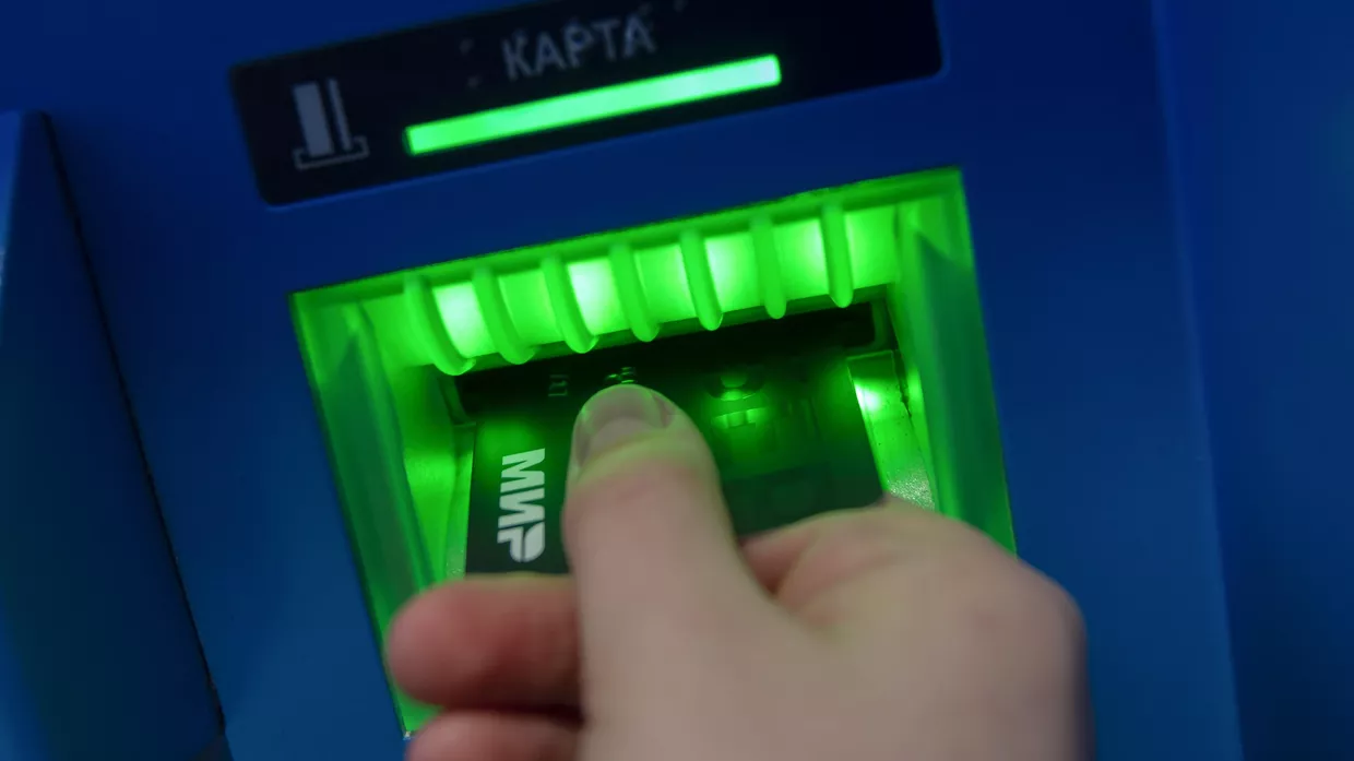 Посетитель с банковской картой МИР у банкомата на территории торгового центра Центральный детский магазин.