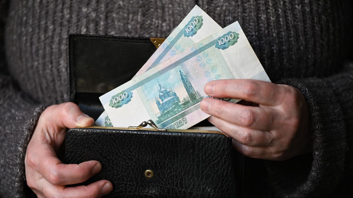 Женщина держит кошелек с тысячными рублевыми купюрами.