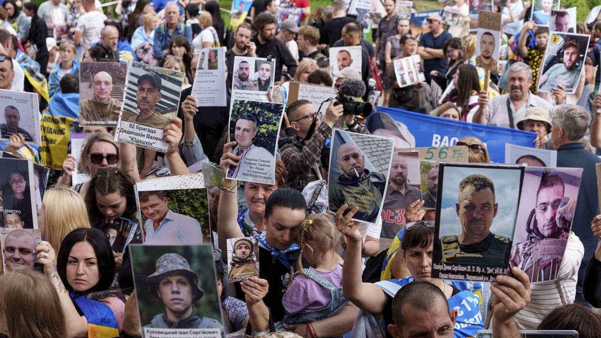 Украинцы держат в руках фотографии своих пропавших на фронте без вести родственников, встречая возвращающихся из плена солдат во время обмена между Россией и Украиной 9 июня 2025 года.