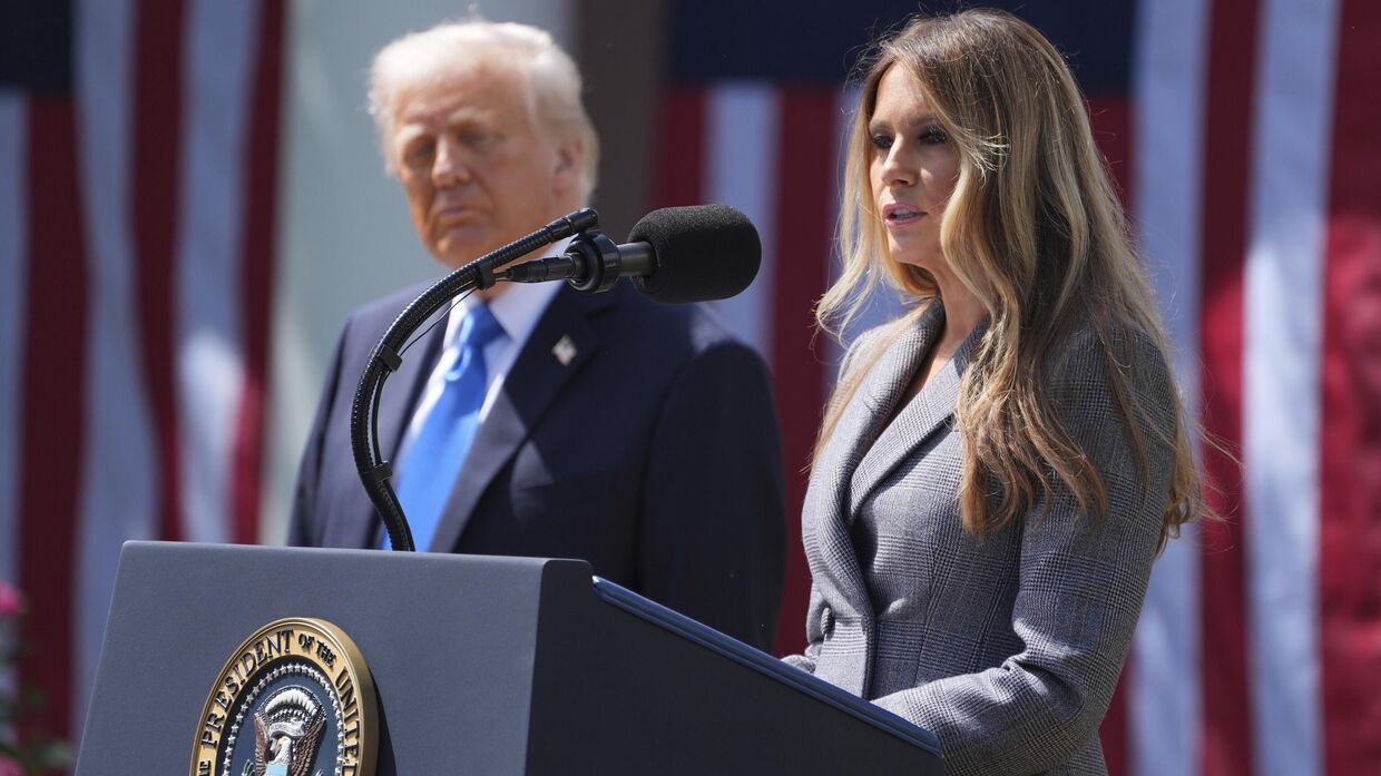 Первая леди Мелания Трамп выступает, а президент Дональд Трамп слушает ее во время церемонии подписания законопроекта в Розовом саду Белого дома