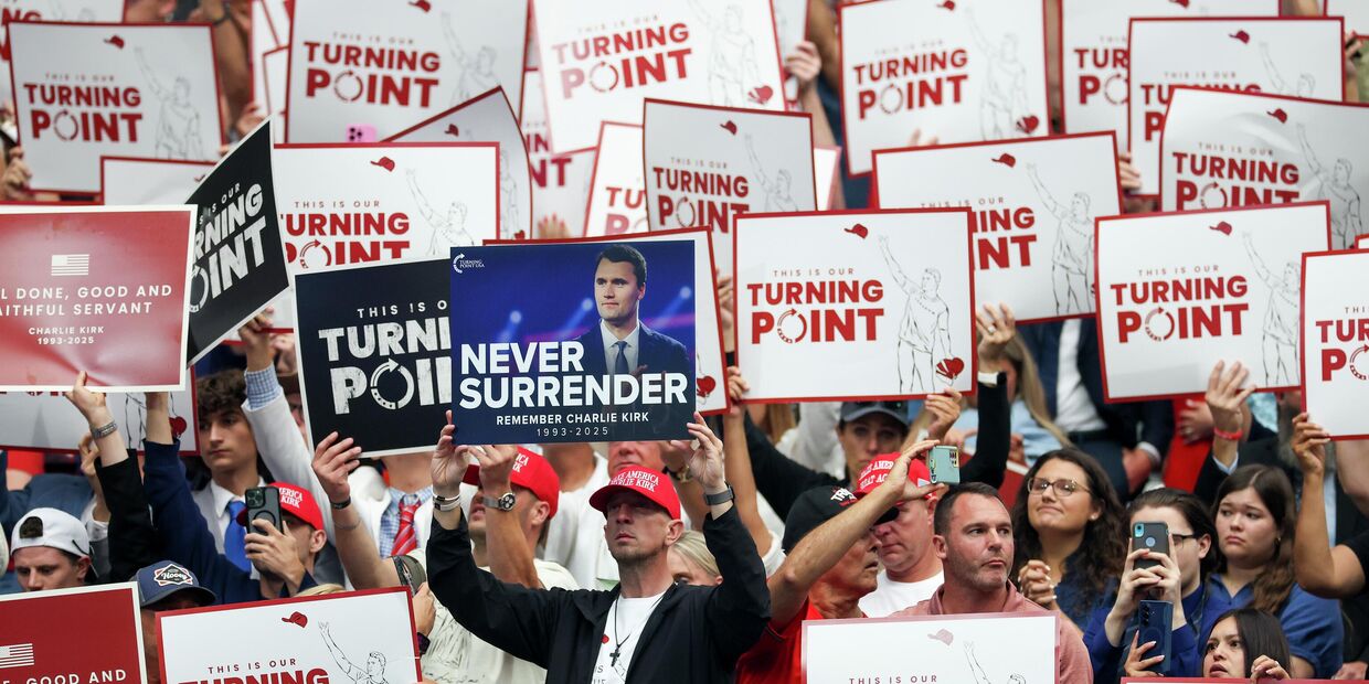 Участники с плакатами на траурной церемонии в память о политическом активисте Чарли Кирке в стадионе State Farm Stadium 21 сентября 2025 года в Глендейле, штат Аризона