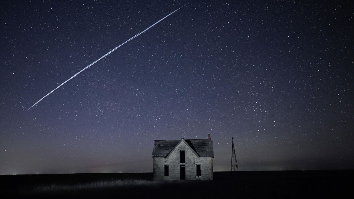 Цепочка спутников SpaceX StarLink пролетает над старым каменным домом 