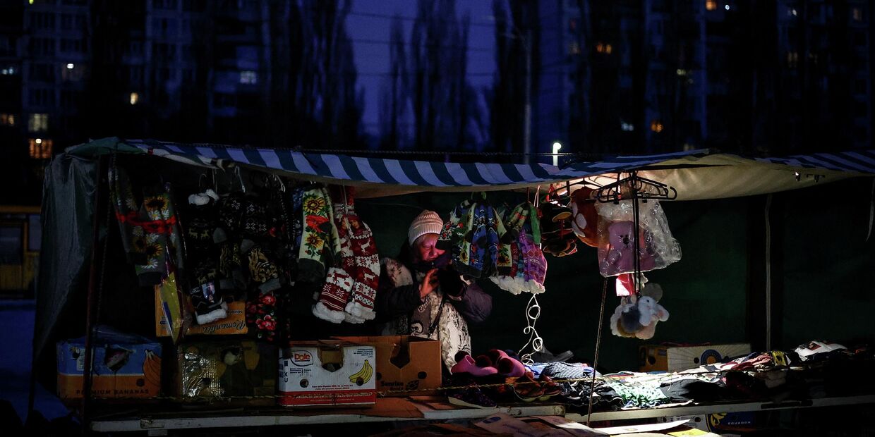 Уличная торговка раскладывает товары в палатке зимним вечером в Киеве