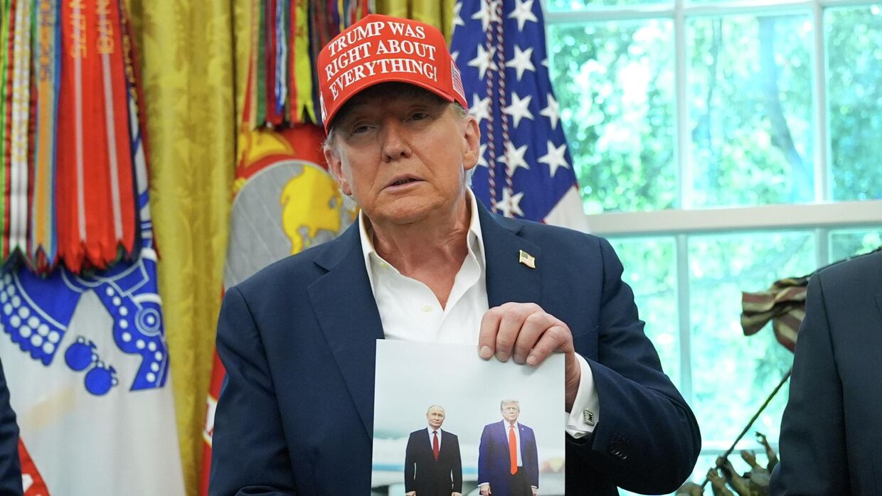 Президент США Дональд Трамп держит в руках свою фотографию с президентом России Владимиром Путиным в Овальном кабинете Белого дома