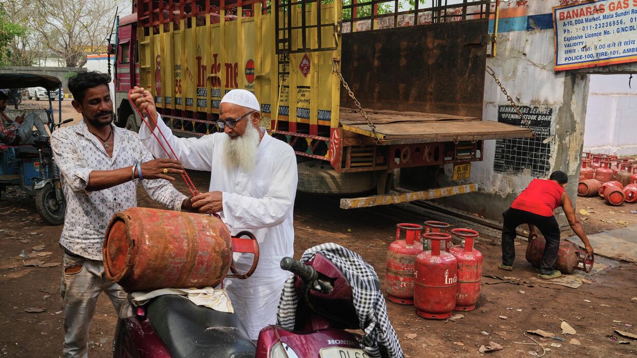 Пожилой мужчина привязывает газовый баллон к своему скутеру в Нью-Дели