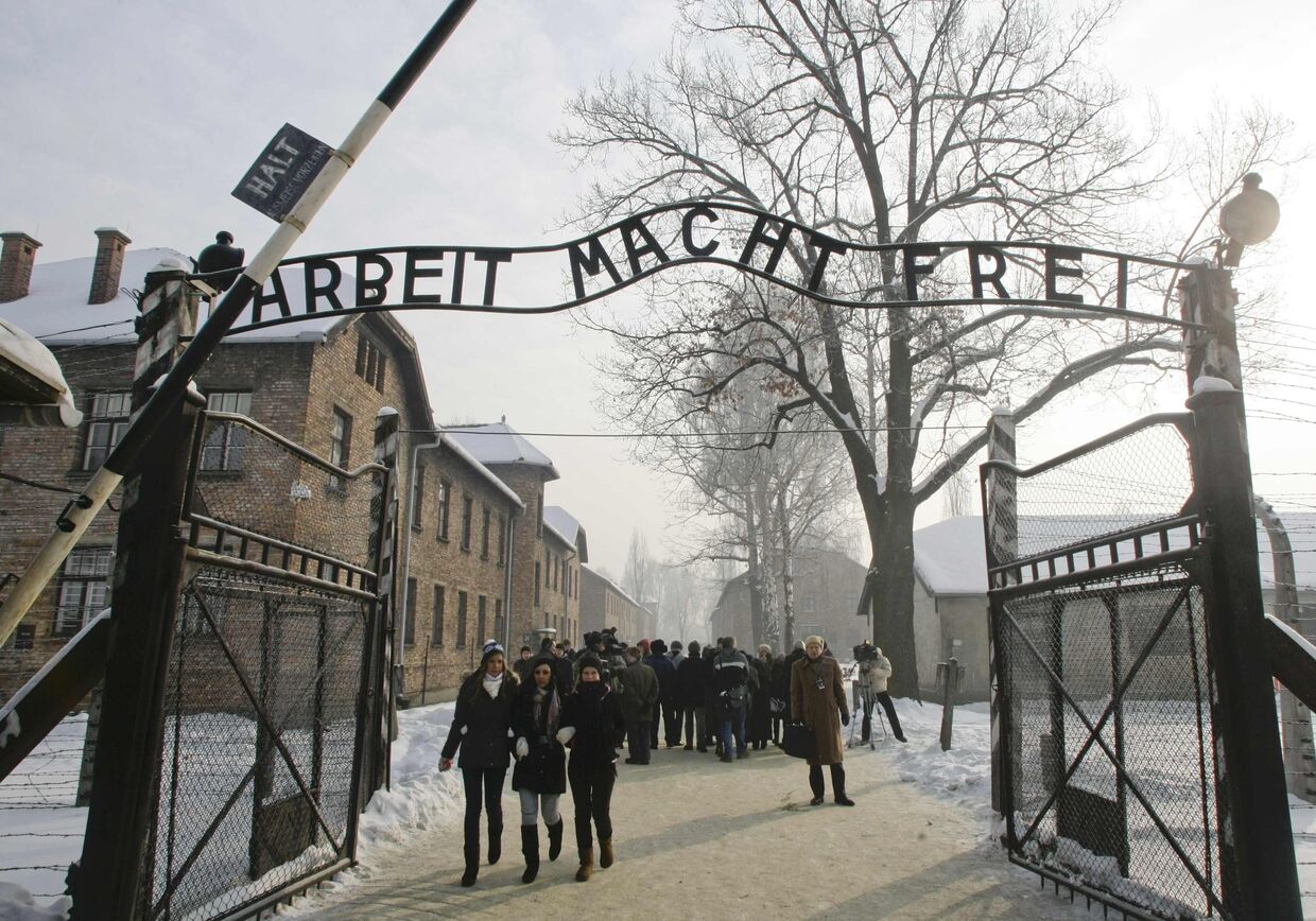 Люди ходят через ворота, с надписью Arbeit Macht Frei (работа освободит вас, бесплатно), бывшего нацистского лагеря смерти Аушвиц в Освенциме