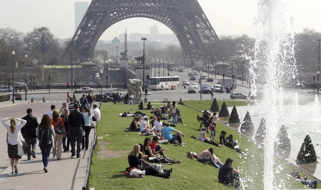 Люди отдыхают на солнце возле Эйфелевой башни в Париже