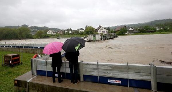 Люди смотрят на последствия наводнения, стоя под зонтами, Швейцария