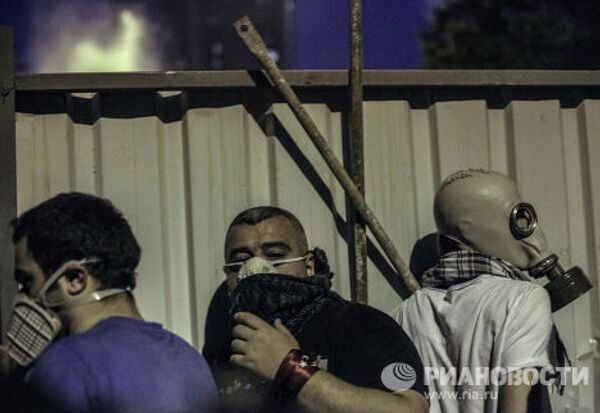 Протестующие прячутся от полиции за забором во время столкновения в Стамбуле