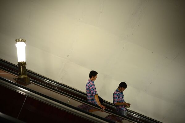Молодые люди в одинаковых рубашках спускаются по эскалатору в московском метро