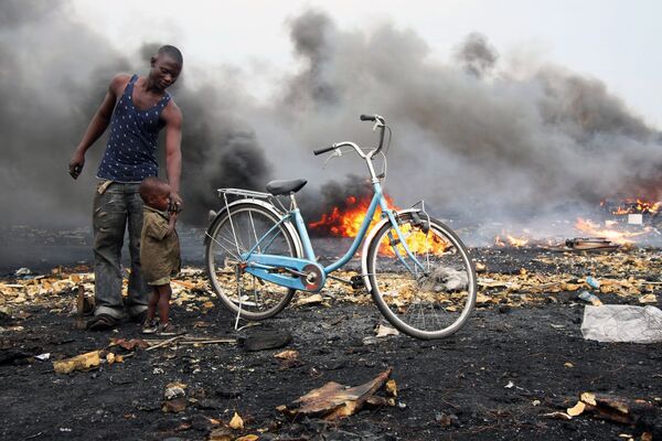 Мужчина с ребенком стоят на фоне дыма в районе Агбогблоши (Agbogbloshie), составляющем агломерацию столицы Ганы