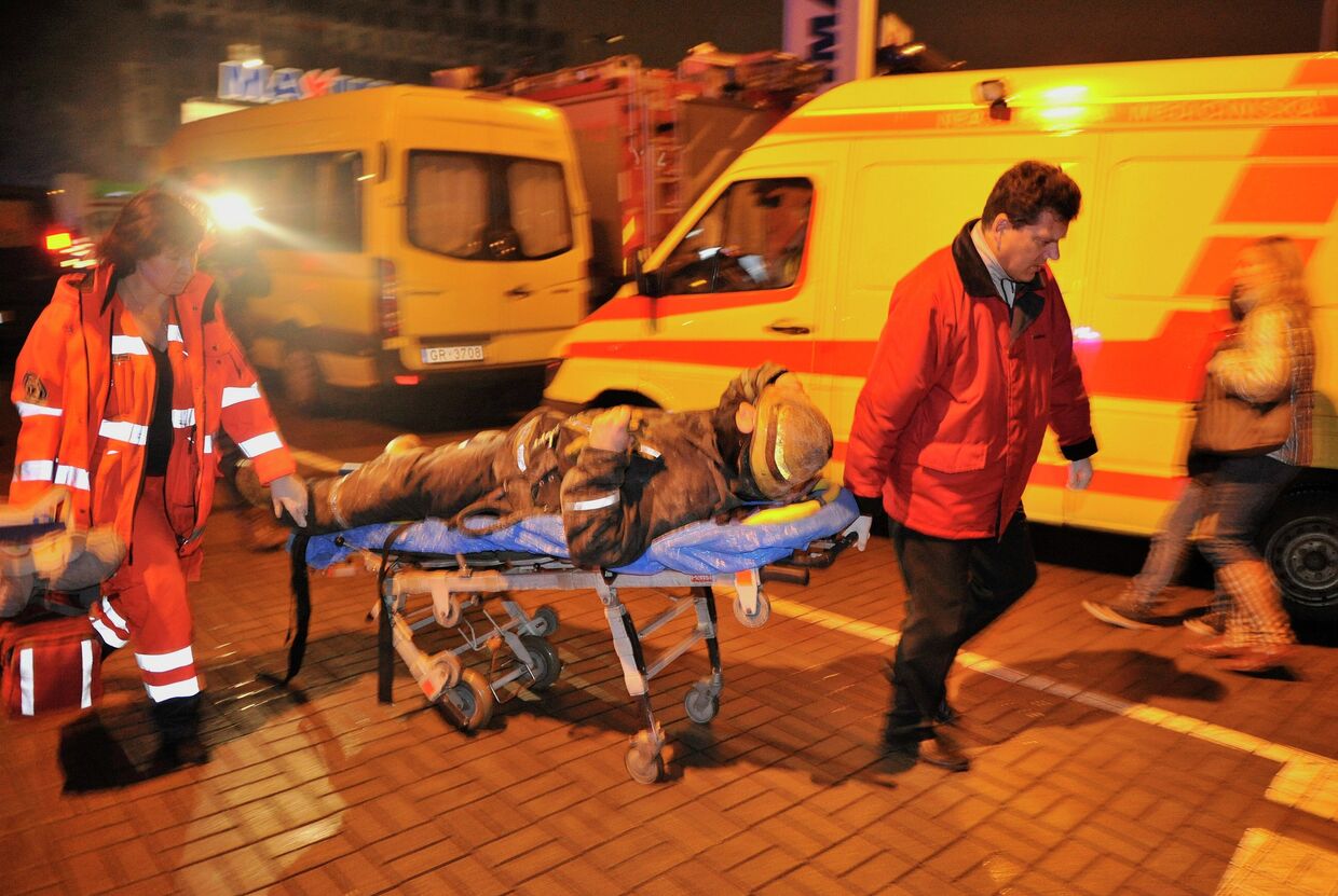 Медики скорой помощи везут носилки с сотрудником пожарно-спасательной службы, пострадавшим при разборе завалов от обрушения крыши в торговом центре Maxima