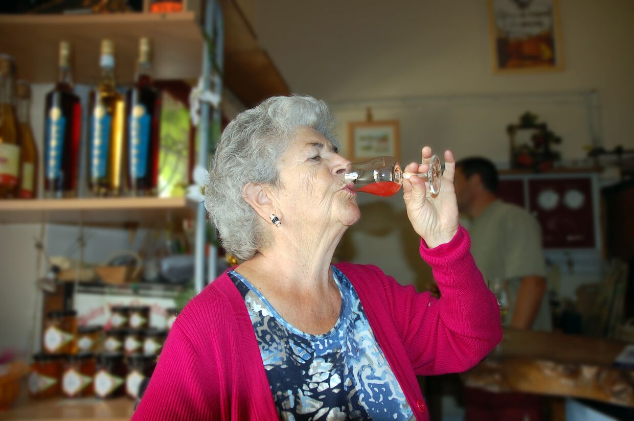 Пожилая женщина пьет алкогольный напиток