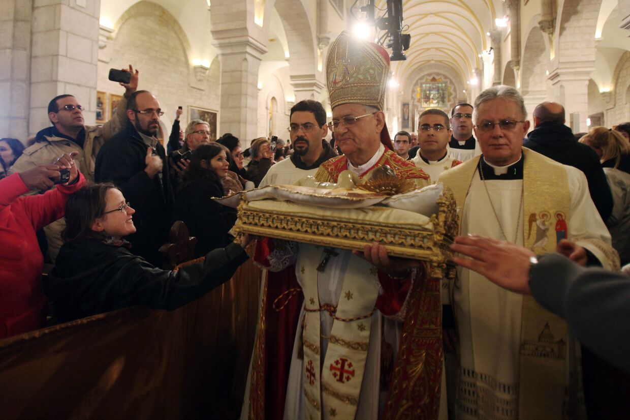 Латинский Патриарх Иерусалима Фуад Туаль несет статуэтку младенца Христа во время рождественской службы в церкви Святой Екатерины в Вифлееме