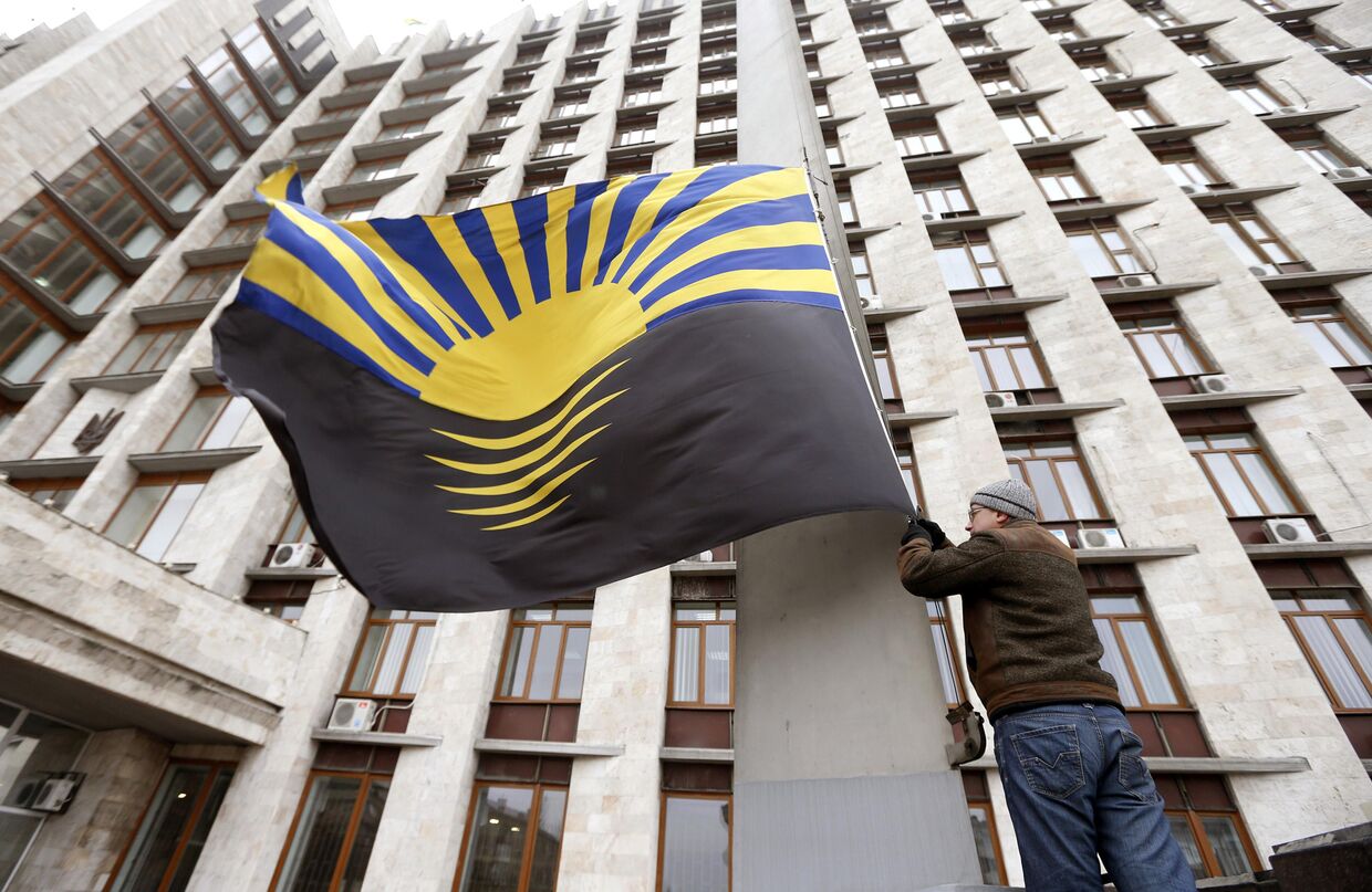 Человек вешает флаг Донецка на здание районной администрации