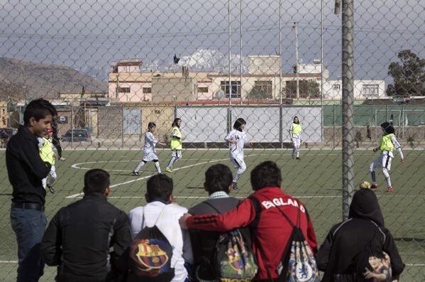 Молодые люди наблюдают за тренировкой женской сборной по футболу на стадионе в Кабуле