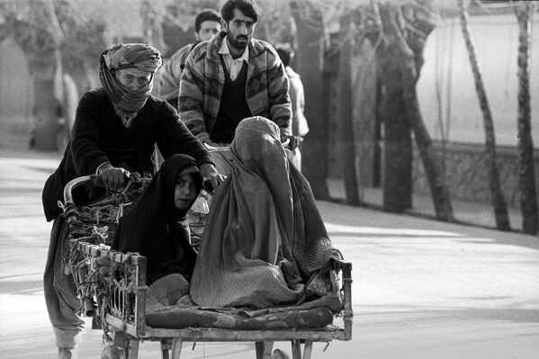 Мужчина толкает повозку, в которой сидят женщина в бурке и девочка в  парандже. Фотография Захры Каземи
