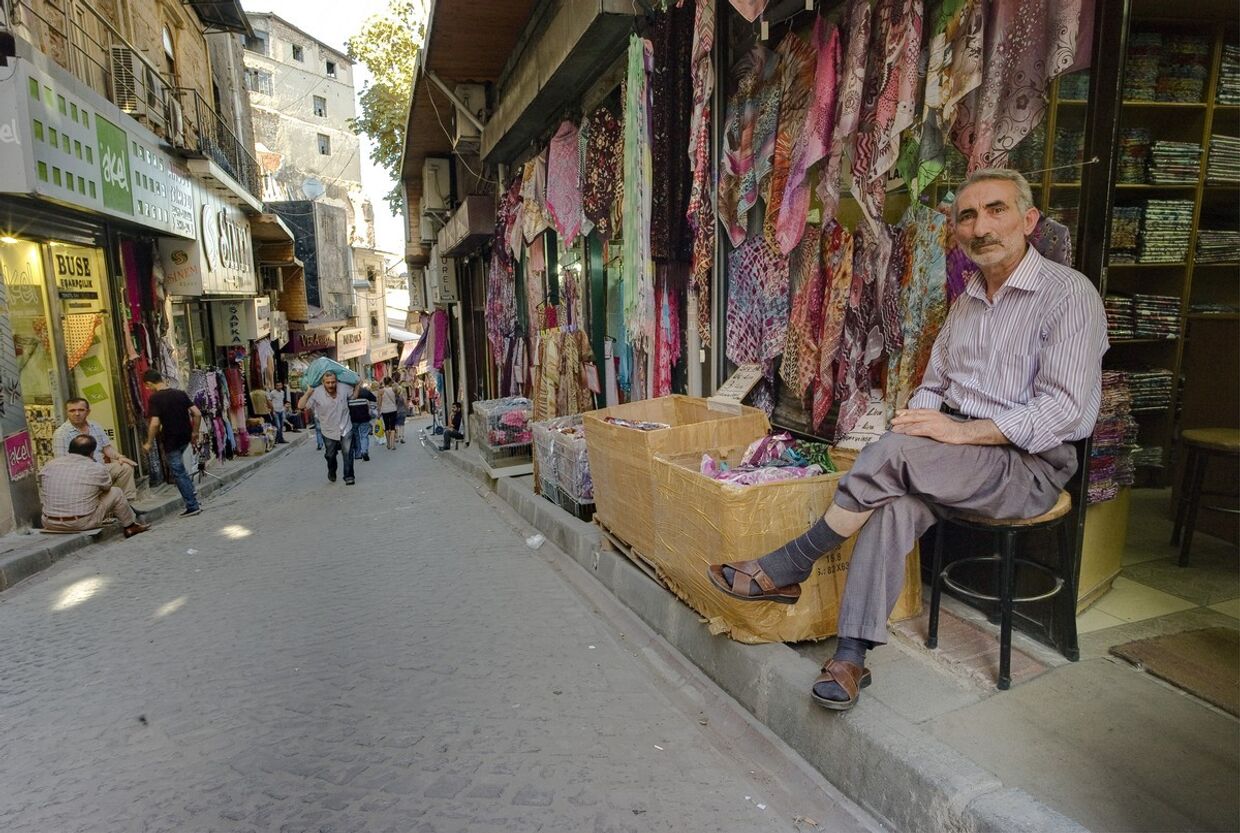 Продавец сидит у входа в свою лавку на улице Стамбула