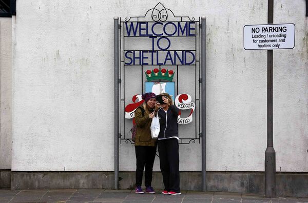 Девушки делают селфи напротив знака «Добро пожаловать в Шетланд» в Леруике